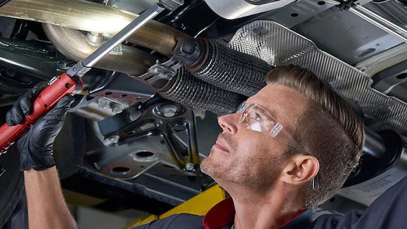 Mechanic wearing gloves checks car engine oil with dipstick in vehicle maintenance.