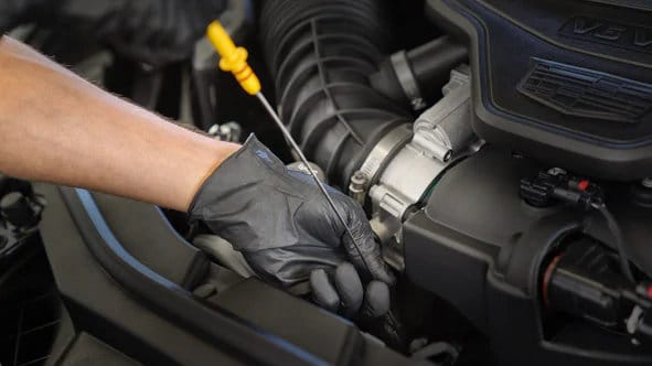 Mechanic wearing gloves checks car engine oil with dipstick in vehicle maintenance.