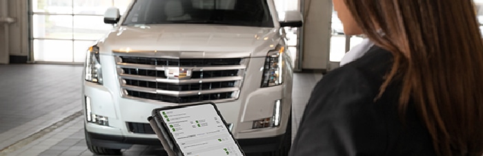 Person using tablet for vehicle diagnostics on a white SUV in a garage.